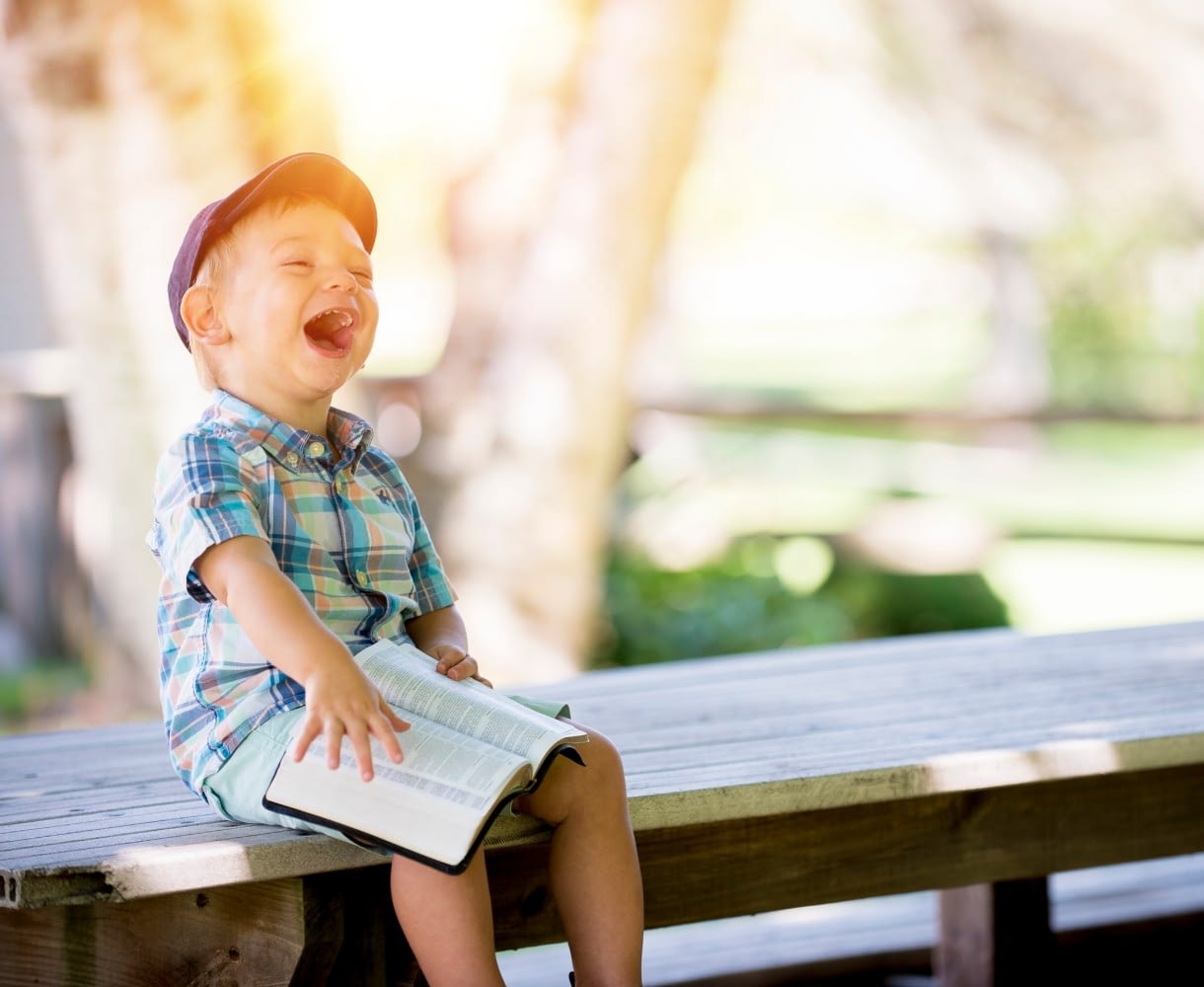 Smiling little boy sitting on a bench hold a book